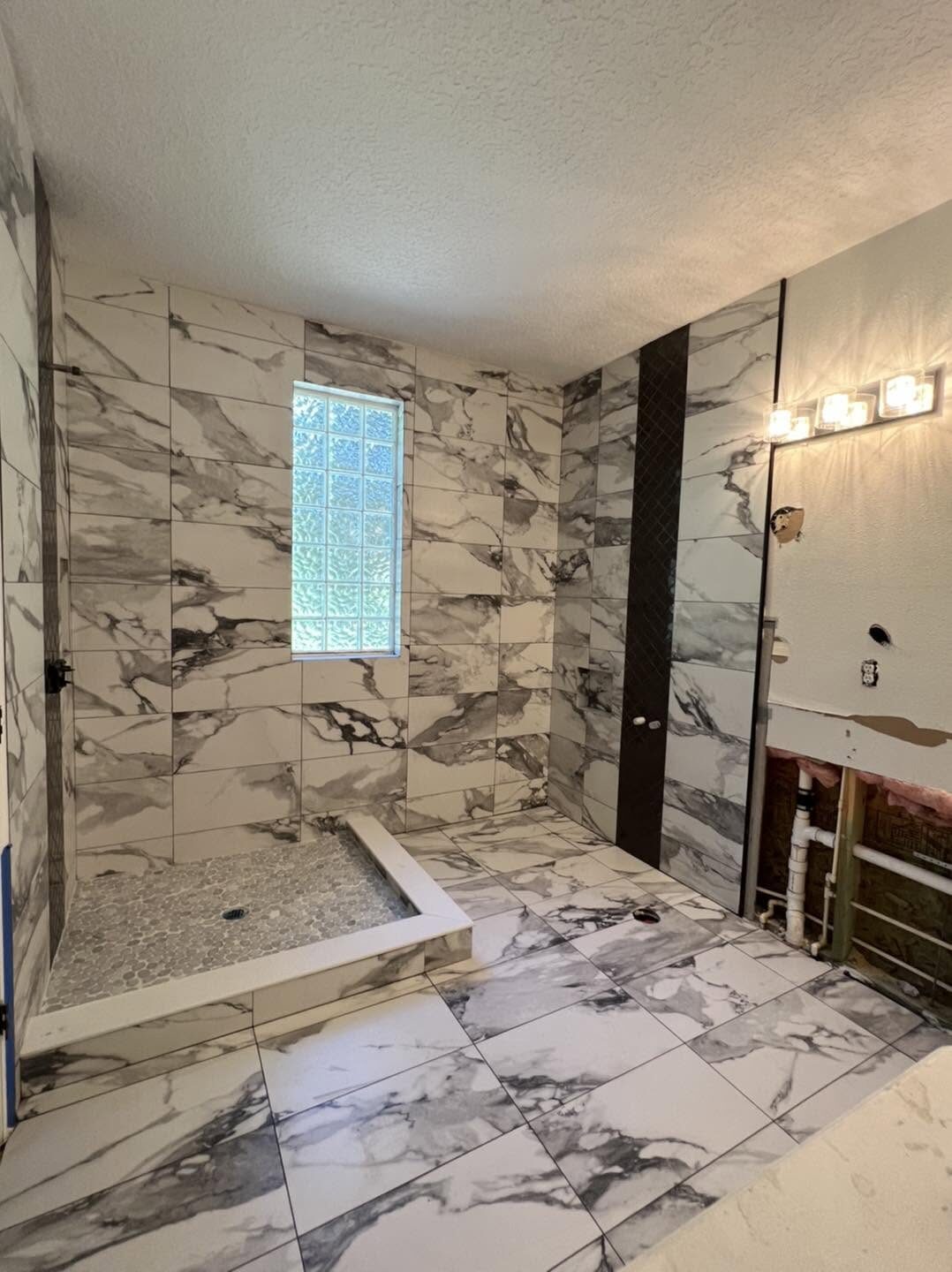 Bathroom with full marble-look tile walls, pebble shower pan and glass block window