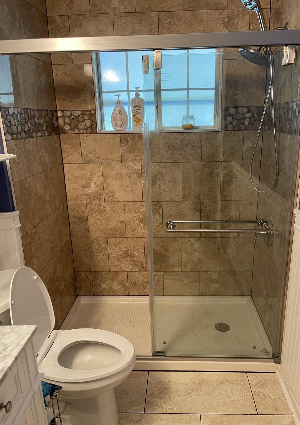 Remodeled bathroom with tiled walk-in shower, river rock accent band and glass doors